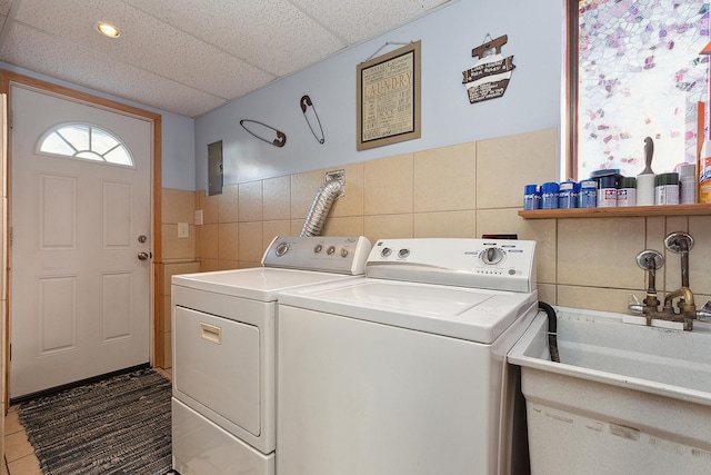 washroom with a sink, electric panel, tile walls, and washer and dryer