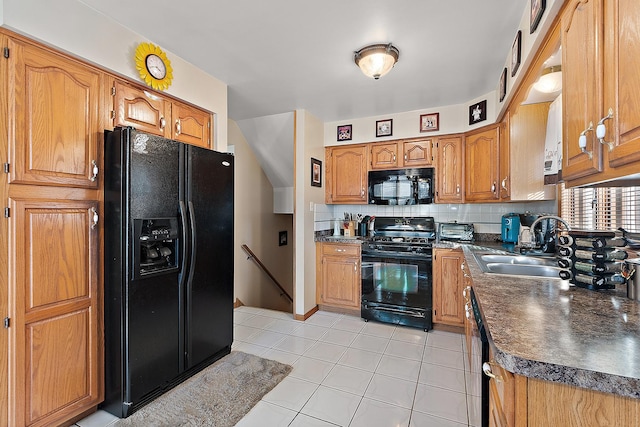 kitchen featuring light tile patterned floors, tasteful backsplash, dark countertops, black appliances, and a sink