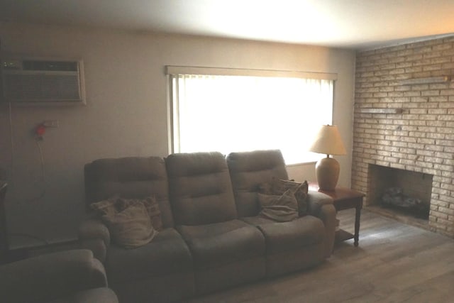 living area with a fireplace, a wall mounted AC, and wood finished floors