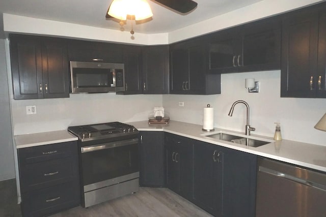 kitchen featuring a sink, light countertops, appliances with stainless steel finishes, dark cabinetry, and light wood-type flooring