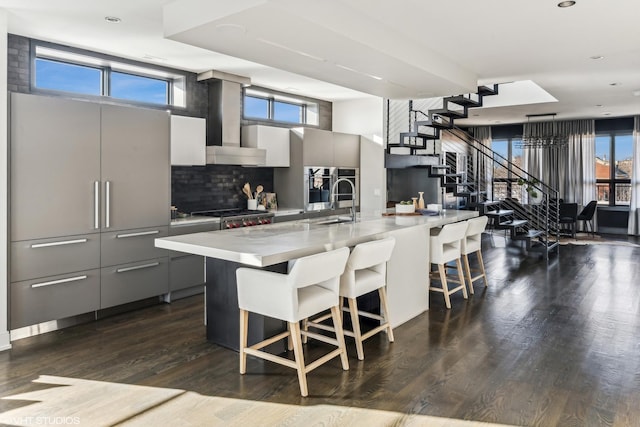 kitchen with plenty of natural light, wall chimney exhaust hood, modern cabinets, a breakfast bar, and gray cabinetry