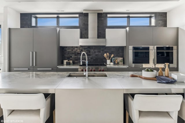 kitchen featuring a breakfast bar area, light countertops, wall chimney range hood, double oven, and high end fridge