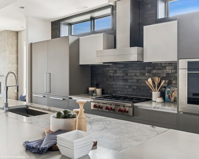 kitchen featuring stainless steel appliances, backsplash, a sink, modern cabinets, and wall chimney exhaust hood