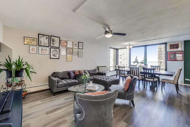 living room featuring a wall unit AC, ceiling fan, baseboard heating, and wood finished floors