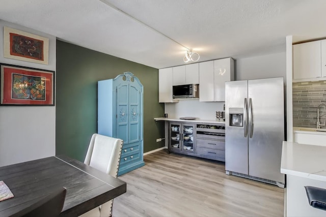 kitchen featuring light wood finished floors, stainless steel appliances, light countertops, white cabinetry, and a sink