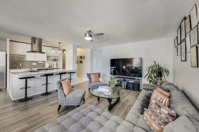 living area featuring light wood finished floors, a ceiling fan, and a textured ceiling