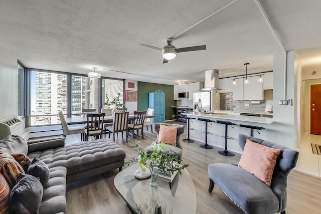 living area with light wood-type flooring, ceiling fan, and a textured ceiling