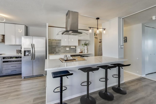 kitchen featuring stainless steel refrigerator with ice dispenser, white cabinetry, a sink, island range hood, and a kitchen bar