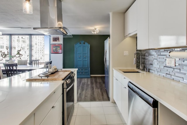 kitchen featuring light tile patterned floors, tasteful backsplash, island exhaust hood, stainless steel appliances, and a sink