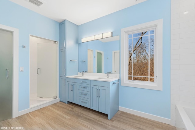 full bath featuring visible vents, a sink, a shower stall, and wood finished floors