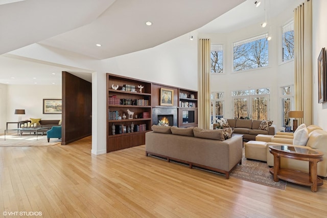 living area with light wood-type flooring, a warm lit fireplace, a high ceiling, and recessed lighting