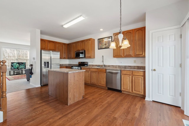 kitchen featuring wood finished floors, appliances with stainless steel finishes, a sink, and a center island