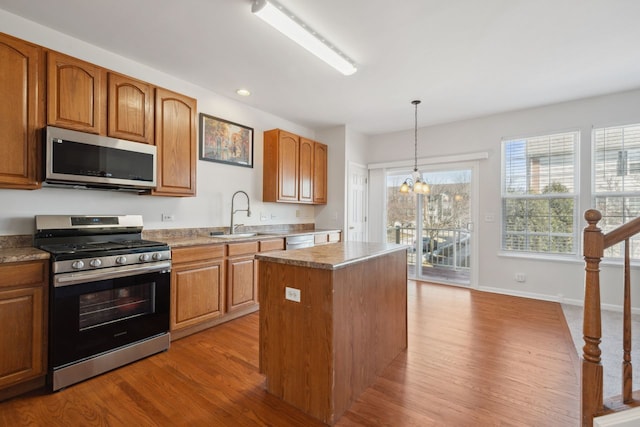 kitchen with a kitchen island, a sink, appliances with stainless steel finishes, light wood finished floors, and decorative light fixtures