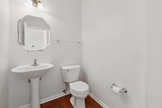 half bathroom featuring baseboards, a sink, toilet, and wood finished floors