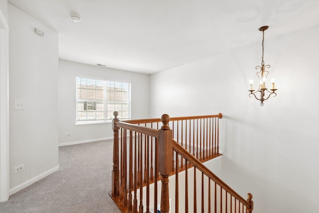 hall featuring carpet, a chandelier, baseboards, and an upstairs landing