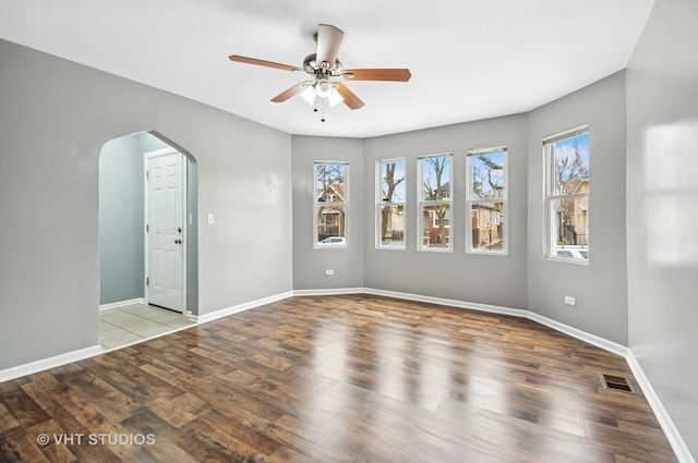 unfurnished room featuring arched walkways, wood finished floors, visible vents, and baseboards