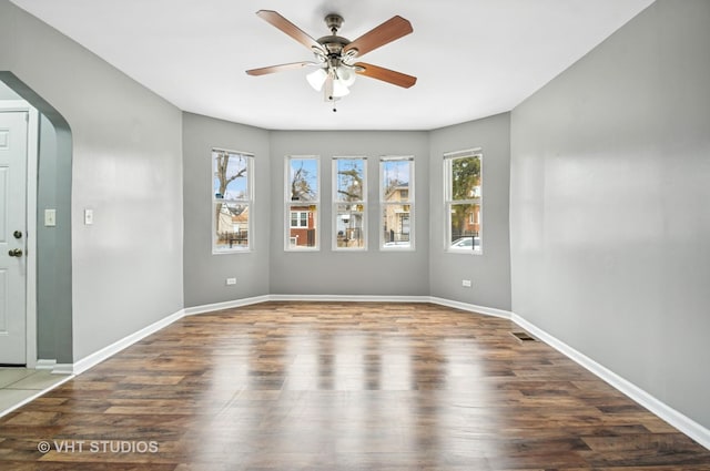 unfurnished room with baseboards, arched walkways, and wood finished floors