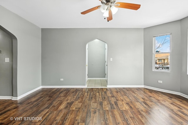 spare room with arched walkways, ceiling fan, baseboards, and wood finished floors