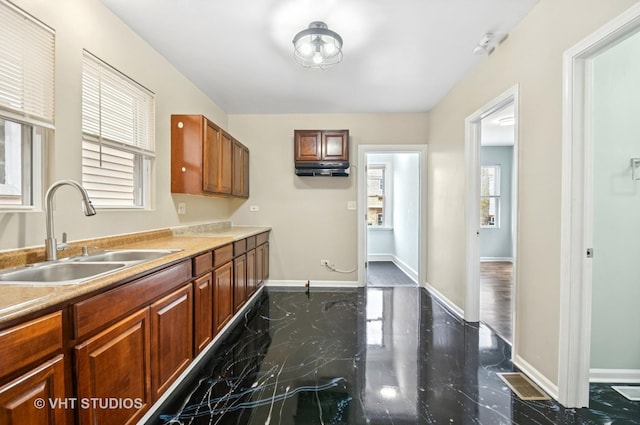 kitchen with marble finish floor, brown cabinetry, a sink, and baseboards