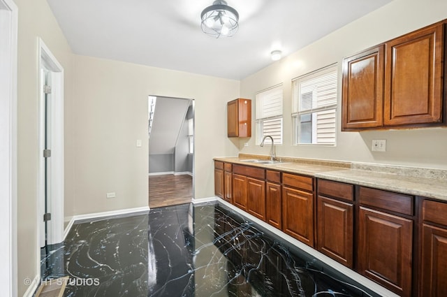 kitchen featuring baseboards, brown cabinets, marble finish floor, light countertops, and a sink