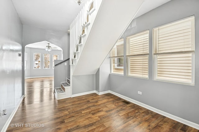 interior space featuring baseboards, stairway, arched walkways, and wood finished floors