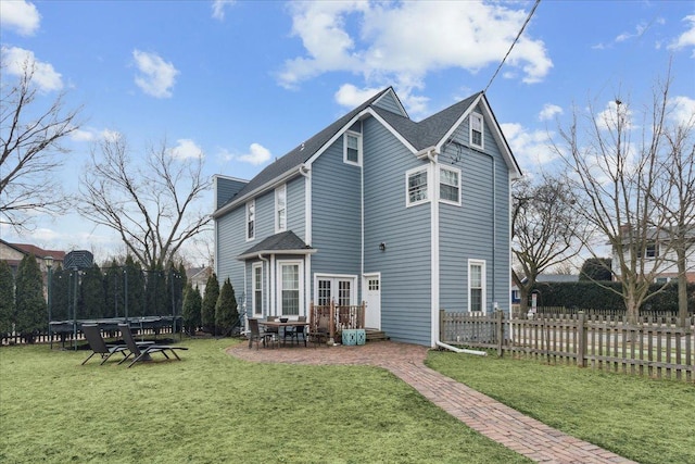 back of property featuring a trampoline, fence private yard, french doors, and a lawn