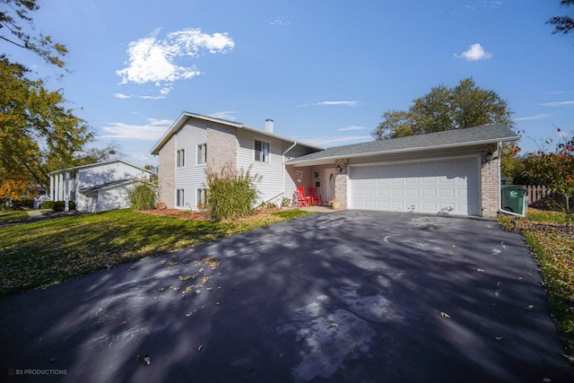 tri-level home with aphalt driveway, a front yard, a chimney, and an attached garage