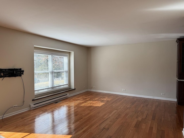 spare room featuring baseboard heating, hardwood / wood-style flooring, and baseboards