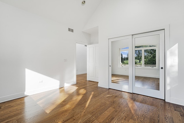 unfurnished bedroom with high vaulted ceiling, wood finished floors, visible vents, and baseboards