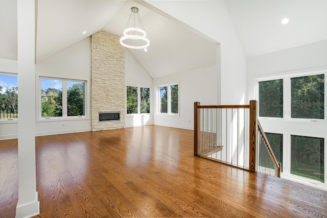 unfurnished living room with a fireplace, high vaulted ceiling, a notable chandelier, and wood finished floors