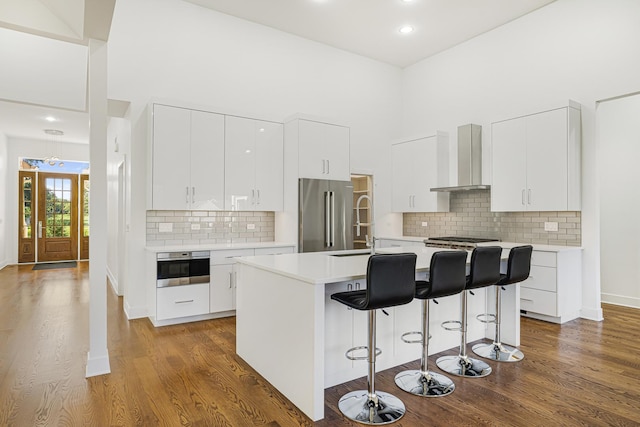 kitchen with stainless steel appliances, light countertops, wall chimney range hood, and dark wood-type flooring