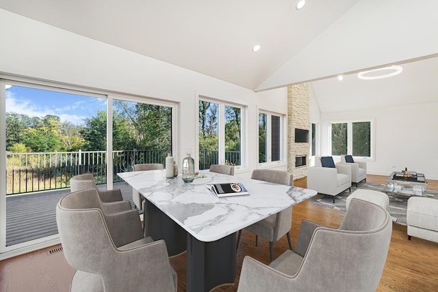 dining room with plenty of natural light, high vaulted ceiling, a fireplace, and wood finished floors