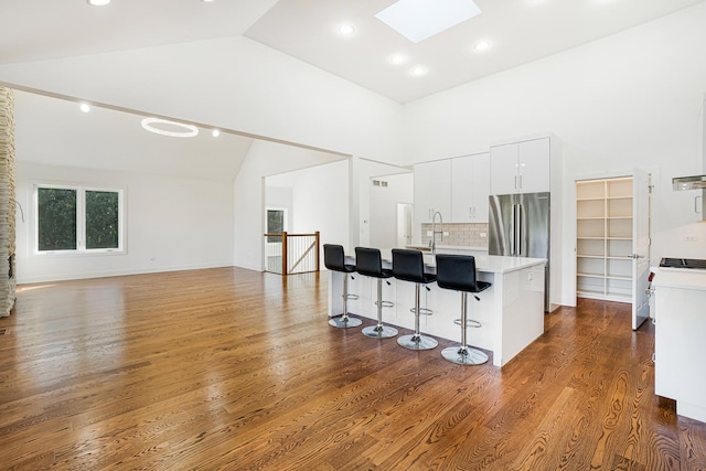 kitchen featuring a skylight, dark wood finished floors, stainless steel refrigerator, a breakfast bar, and light countertops