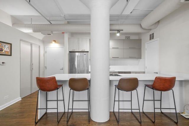 kitchen featuring dark wood-type flooring, visible vents, a kitchen breakfast bar, light countertops, and freestanding refrigerator