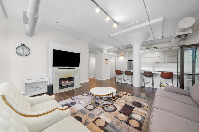 living room with a warm lit fireplace, dark wood finished floors, and track lighting