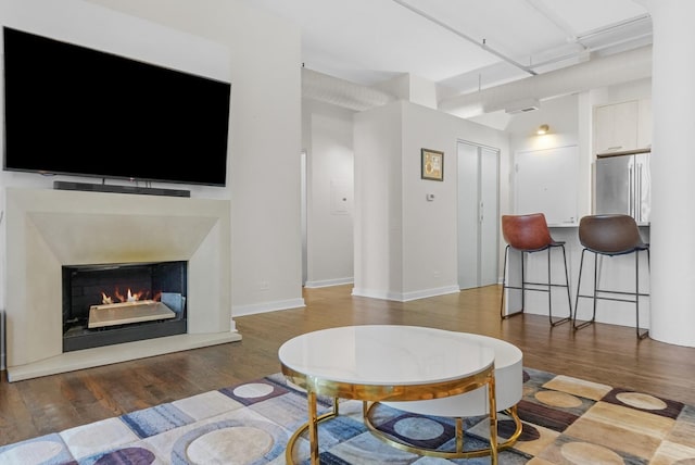 living area with a warm lit fireplace, baseboards, and wood finished floors