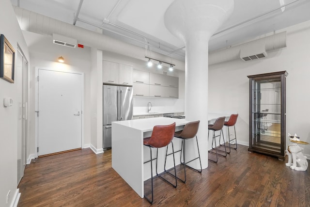 kitchen with high quality fridge, a sink, visible vents, dark wood-style floors, and a kitchen bar