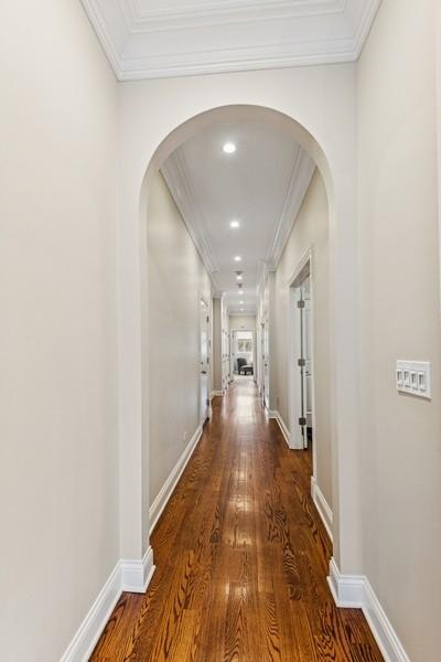 hall featuring arched walkways, ornamental molding, wood finished floors, and baseboards