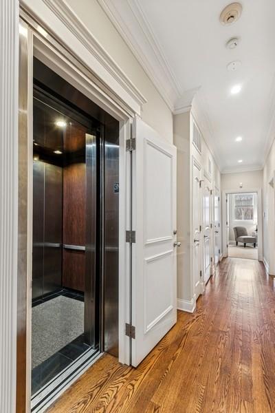 hallway with elevator, ornamental molding, wood finished floors, and baseboards