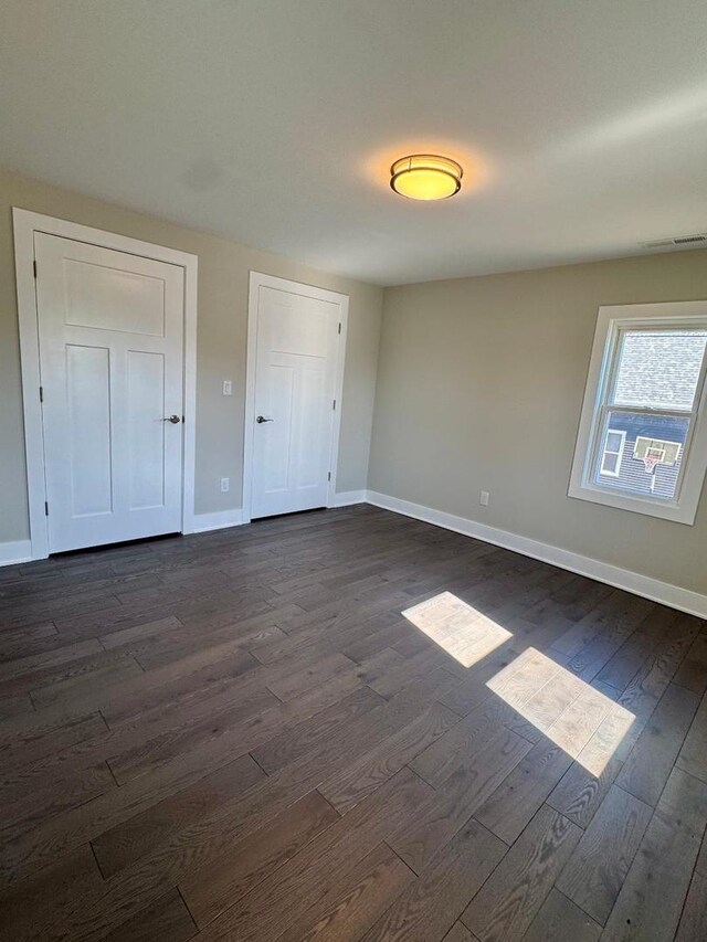 unfurnished bedroom with dark wood finished floors, visible vents, and baseboards