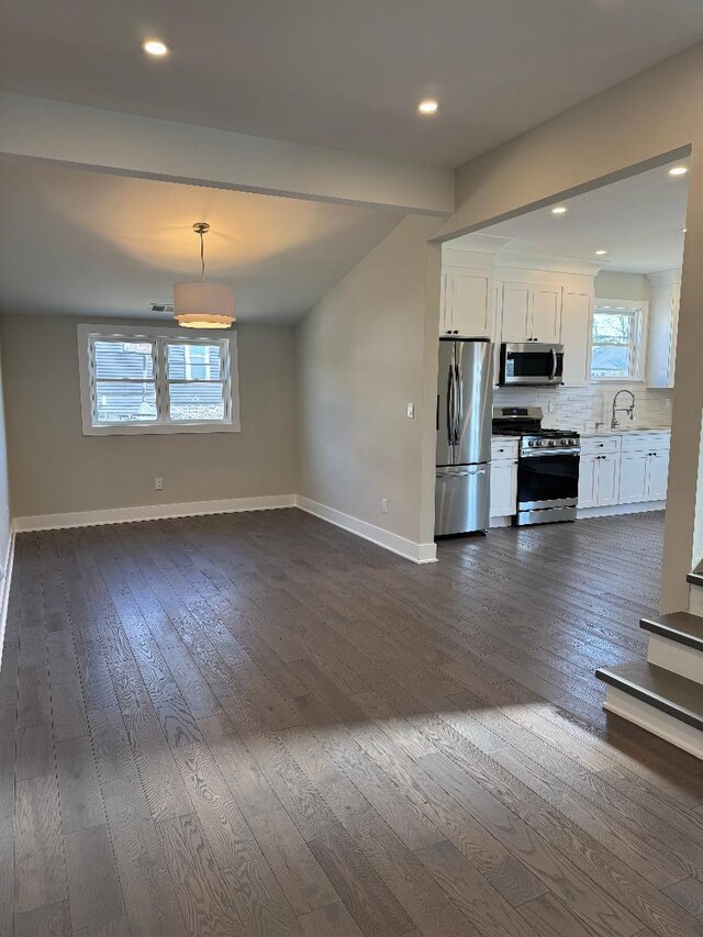 kitchen featuring a sink, backsplash, white cabinetry, appliances with stainless steel finishes, and baseboards