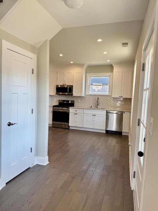 kitchen featuring a sink, backsplash, appliances with stainless steel finishes, white cabinets, and dark wood-style flooring