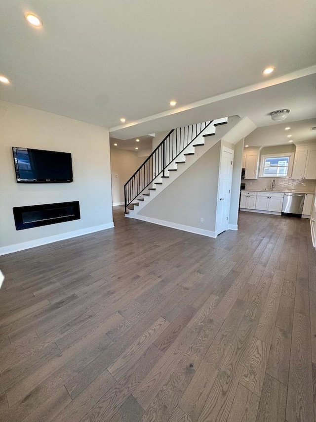 unfurnished living room featuring stairway, baseboards, and dark wood finished floors