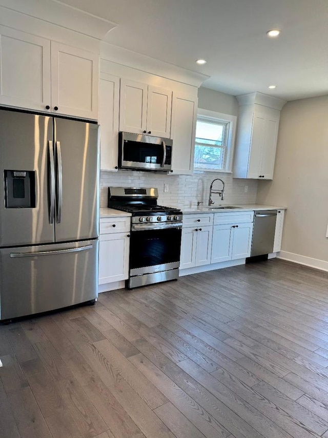 kitchen featuring dark wood-type flooring, a sink, tasteful backsplash, appliances with stainless steel finishes, and light countertops