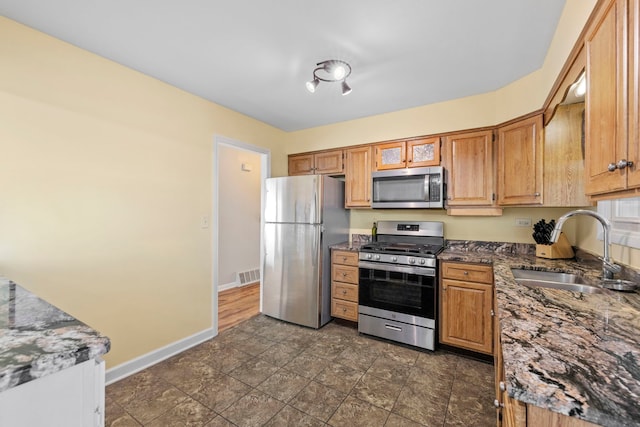 kitchen featuring visible vents, appliances with stainless steel finishes, a sink, dark stone counters, and baseboards