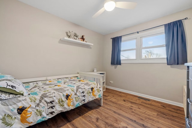 bedroom with a ceiling fan, visible vents, baseboards, and wood finished floors