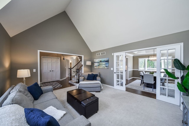 carpeted living room featuring visible vents, baseboards, high vaulted ceiling, stairway, and french doors