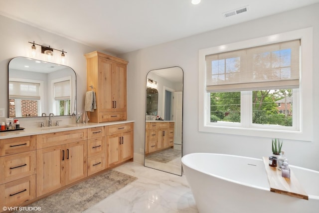 bathroom with marble finish floor, visible vents, a freestanding tub, and vanity