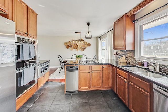 kitchen with a peninsula, a sink, appliances with stainless steel finishes, tasteful backsplash, and dark countertops