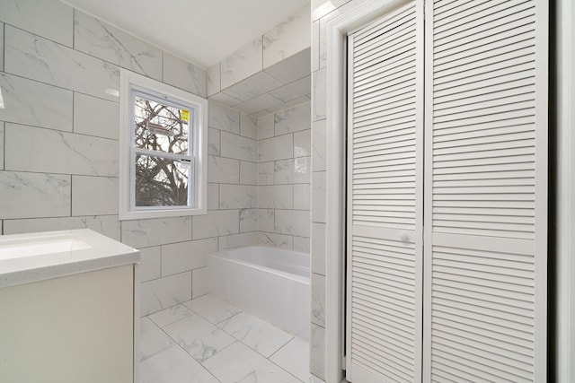 full bath with a tub, vanity, a closet, marble finish floor, and tile walls